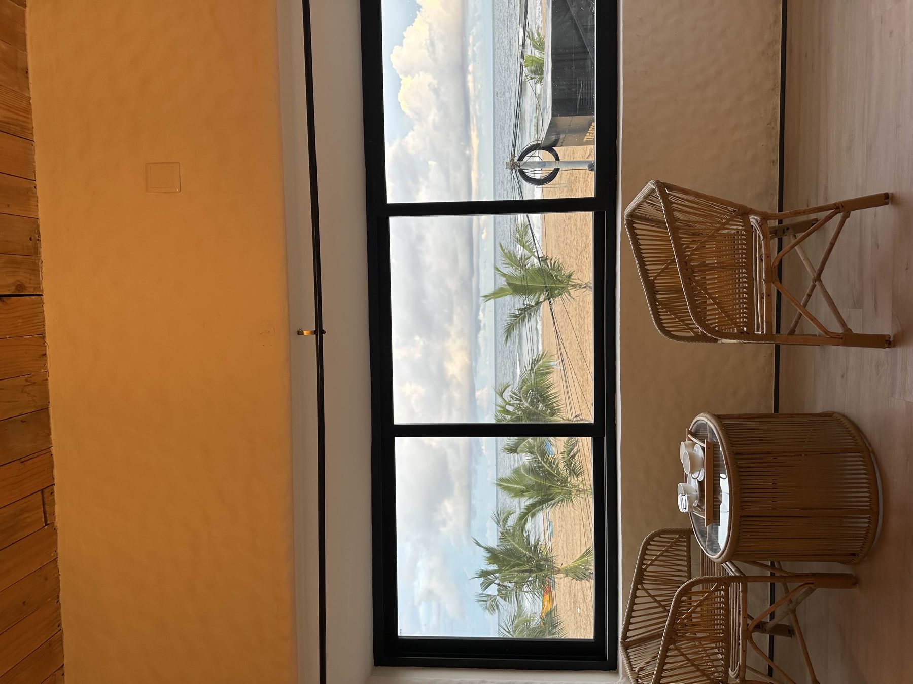 Rattan lounge seating beside floor-to-ceiling windows overlooking the beach